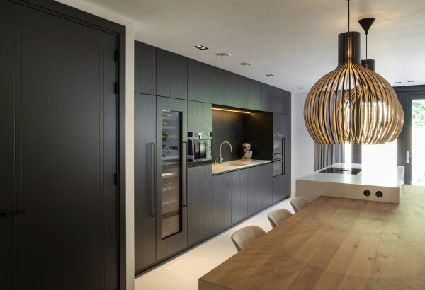 Moderne keuken in eiken fineer met Corian werkblad en Fenix Angola achterwand, naast een ruime houten eettafel